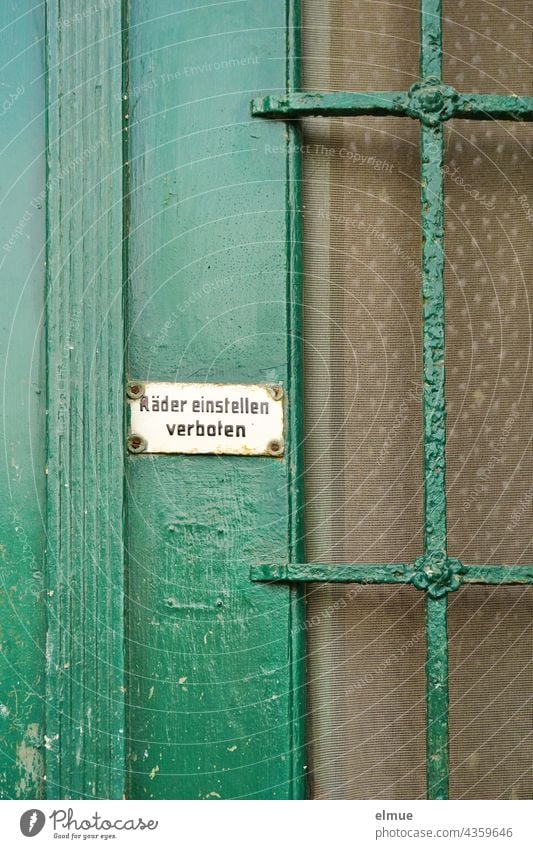 On an old, green painted front door with glass part is a small white sign with the inscription - wheels adjust forbidden - fastened / live / nostalgia