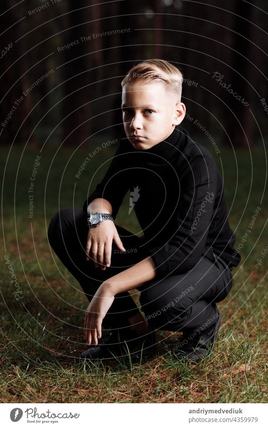 Stylish attractive young guy with a fashionable hairstyle in a trendy black outfit enjoys an outdoor vacation in the park. man sunglasses forest standing sexy