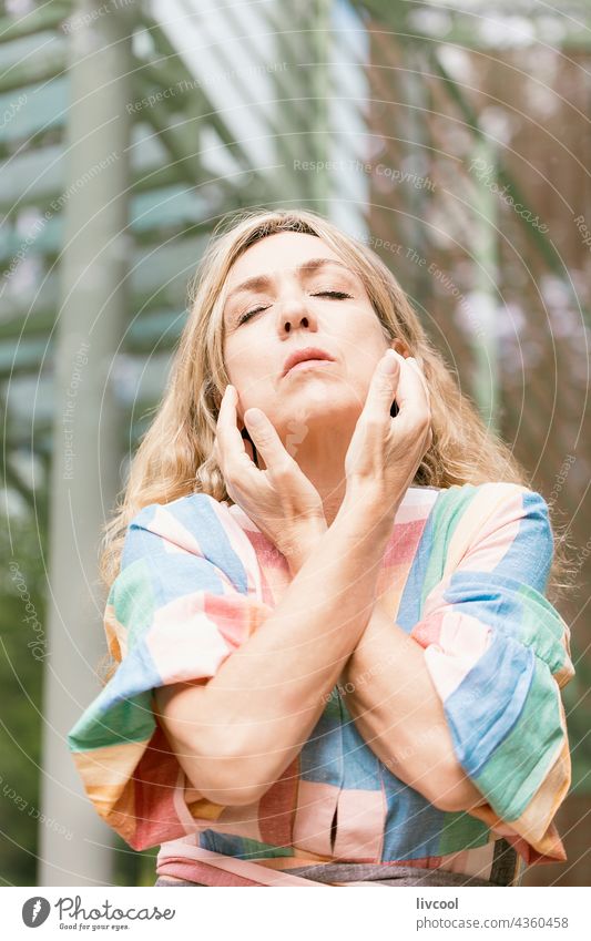 woman approaching her hands to her face in a romantic attitude portrait performance arty blonde dress nature bridge tree park garden exterior san sebastian