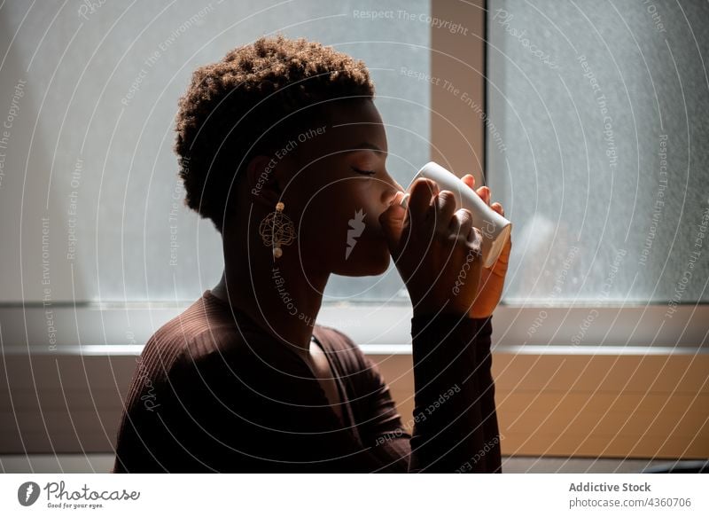 Black woman drinking coffee from cup at home morning refreshment beverage enjoy tasty sunny female ethnic black african american mug tea cozy short hair calm