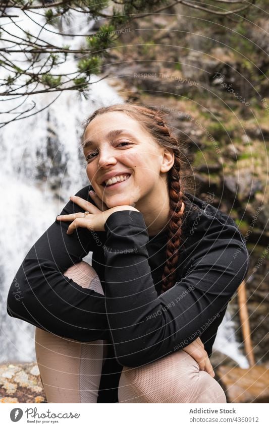 Delighted traveling woman looking at camera against waterfall traveler hiker smile forest mountain adventure happy female pyrenees journey woods highland