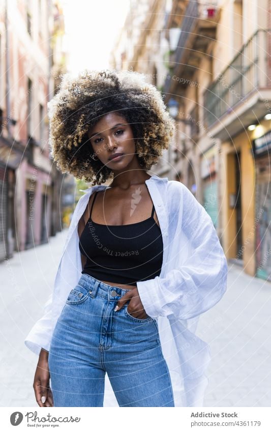 Black woman standing on street looking at camera serious urban millennial posture female beautiful building casual attractive brunette long hair hairstyle