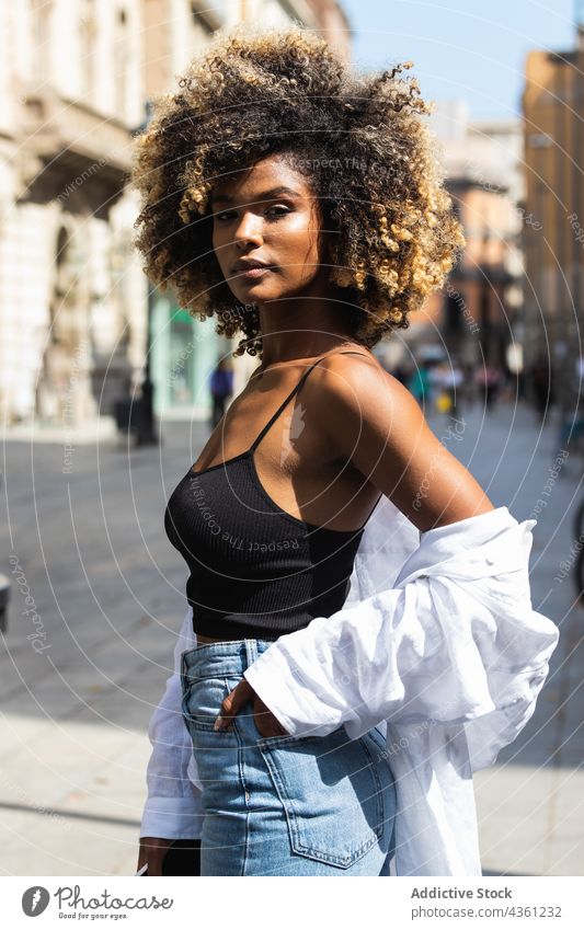 Black woman standing on street looking at camera serious urban millennial posture female beautiful building casual attractive brunette long hair hairstyle