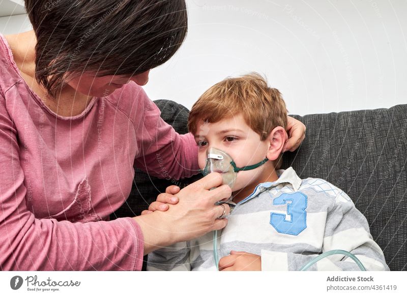 Mother putting on oxygen mask on face of child for inhalation mother put on inhale procedure sick ill breathe together home son parent care kid content help