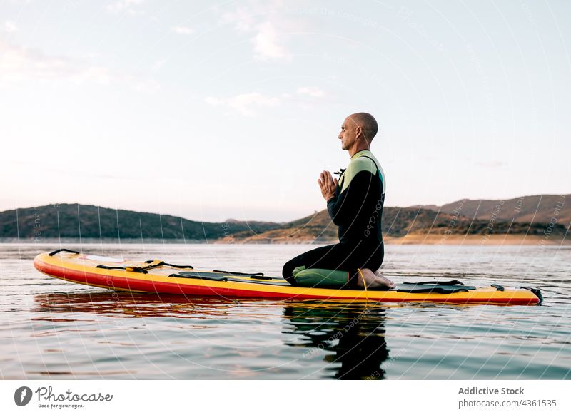 Man practicing yoga on SUP board in sea man paddleboard meditate sup board practice thunderbolt pose namaste evening male surfer water asana sunset calm healthy