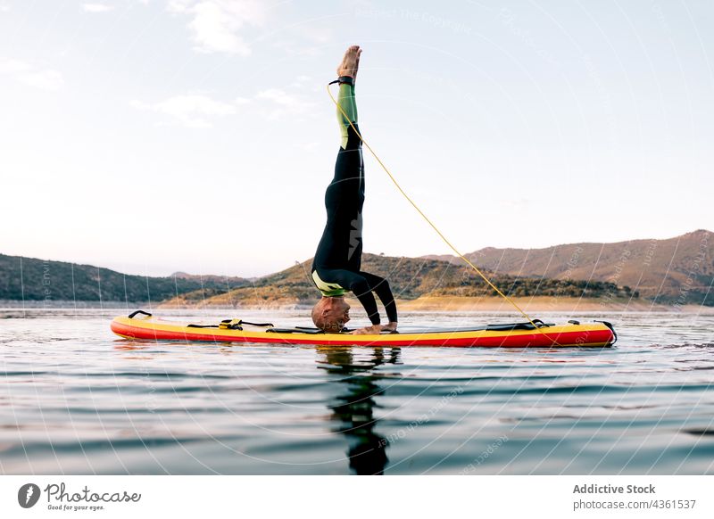 Man doing yoga on paddleboard in sea man sup board headstand pose practice balance asana male surfer sunset surfboard ocean evening twilight activity