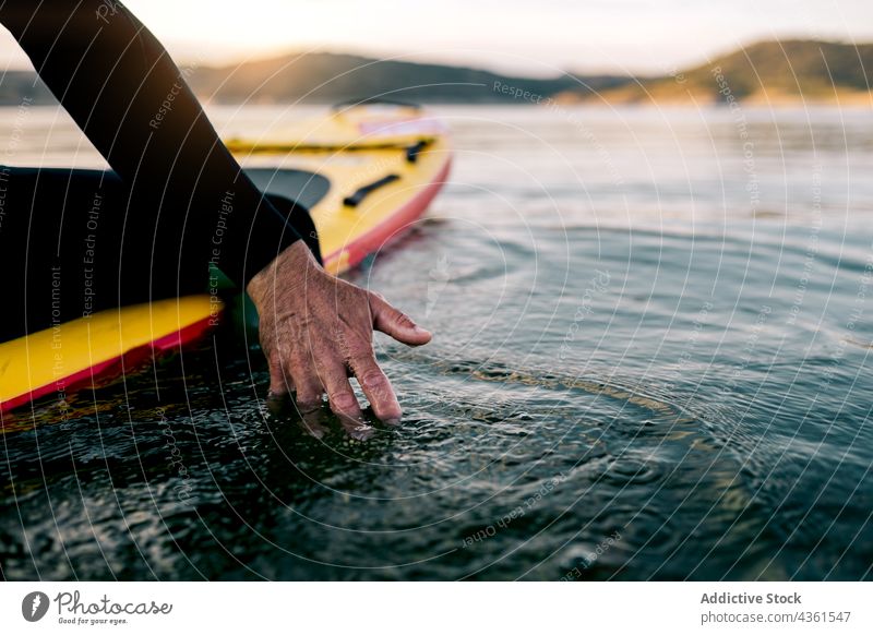 Crop man on paddleboard touching sea water sup board surfer sunset summer peaceful male evening ripple surface calm ocean surfboard sport hobby sundown relax