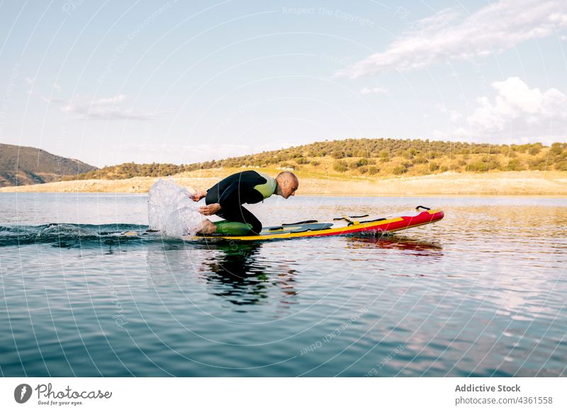 Man on paddle board floating on lake man paddleboard sport kneel activity practice male active sporty adult water sports hobby recreation swim lifestyle energy