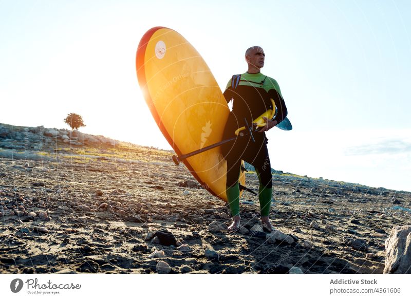 Sporty man with paddle board standing on beach paddleboard confident activity practice training challenge male active sporty middle age mature water sports