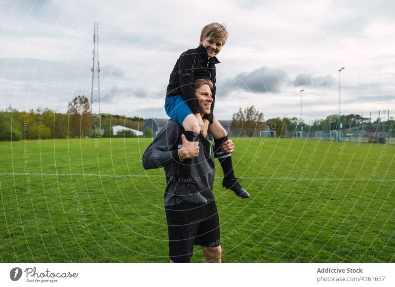 Father and son playing football in field father together carrying shoulder teenage player soccer boy game activity having fun grass parent fatherhood parenthood