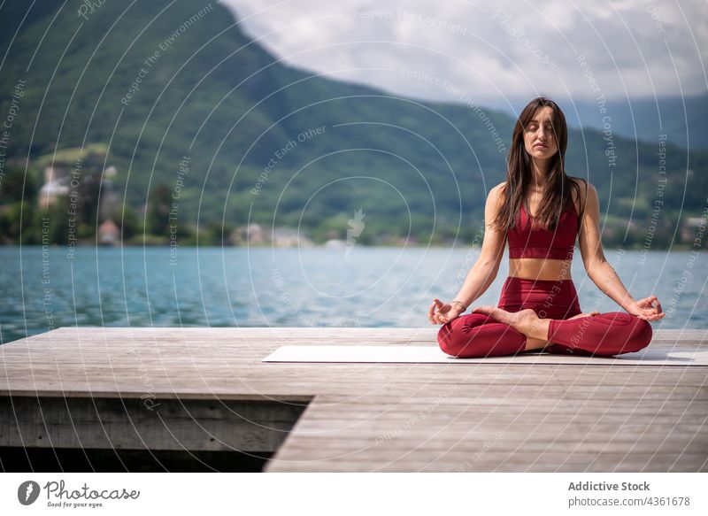 Flexible woman meditating in Lotus pose on pier meditate yoga lotus pose padmasana lake serene practice female water healthy tranquil sit vitality quiet