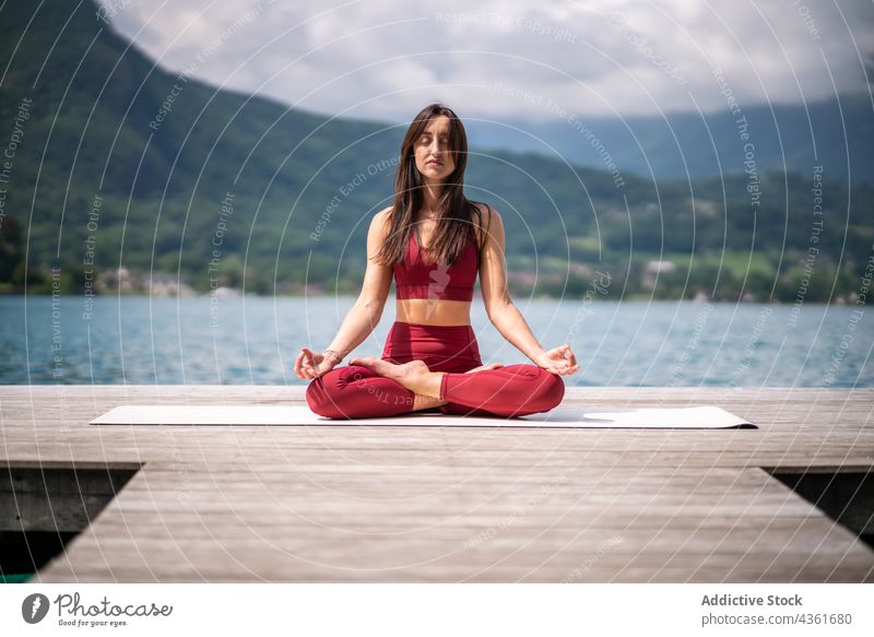 Flexible woman meditating in Lotus pose on pier meditate yoga lotus pose padmasana lake serene practice female water healthy tranquil sit vitality quiet