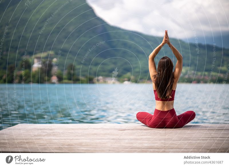 Anonymous flexible woman meditating in Lotus pose on pier meditate yoga lotus pose padmasana lake serene practice female water healthy mudra sit vitality