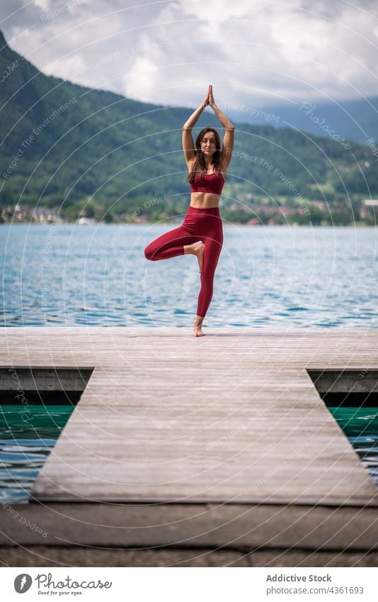 Slender woman doing yoga in Tree pose on pier tree pose practice lake balance vrksasana flexible female wellness arms raised pond nature quay vitality