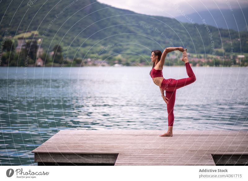 Flexible woman doing yoga in Lord of the Dance Pose on quay balance practice pose tuladandasana lake pier female virabhadrasana water tranquil calm vitality zen