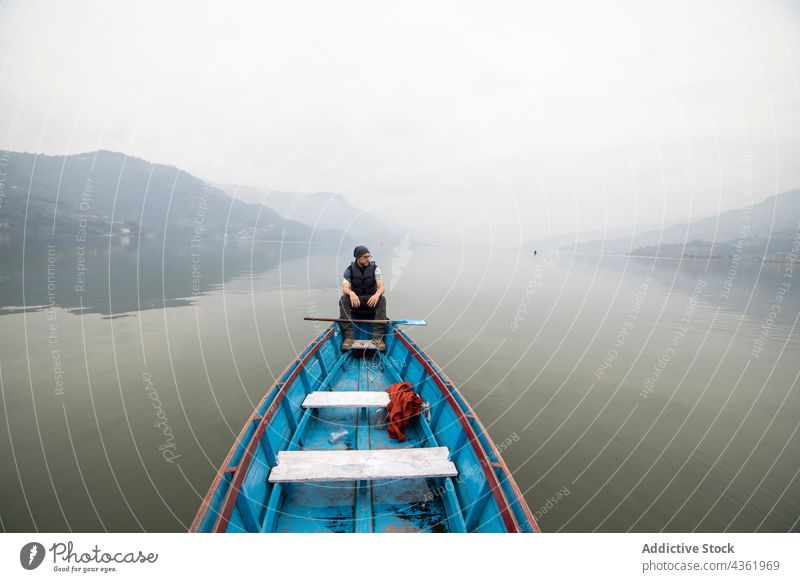 Traveling man floating in boat on lake in foggy morning traveler mist pond mountain male nepal vacation water tranquil calm haze nature highland wooden sit