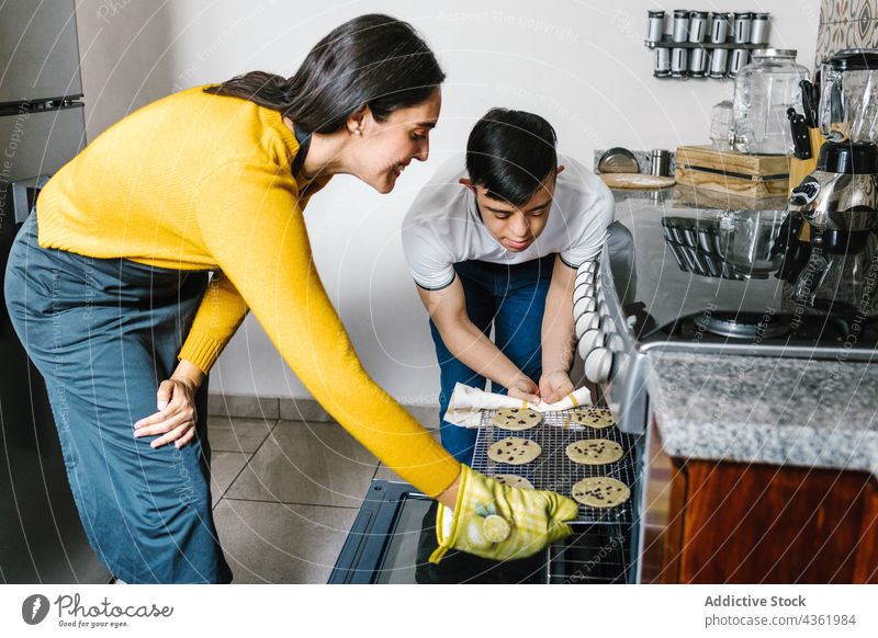 Content Latin mother and son with Down syndrome preparing cookies in kitchen together down syndrome oven help cheerful boy ethnic latin sweet home food bake