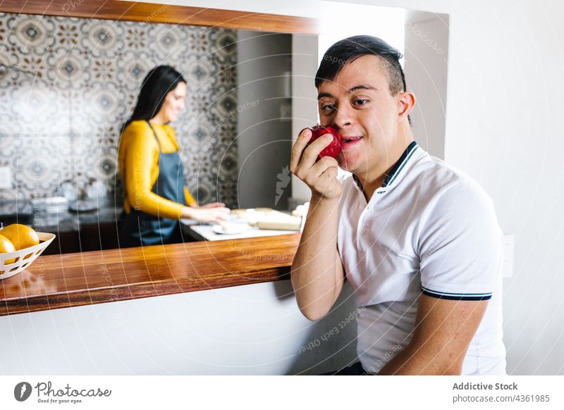 Smiling ethnic boy with Down syndrome eating fresh apple in kitchen down syndrome ripe fruit disorder mental enjoy latin teenage mother together happy sit