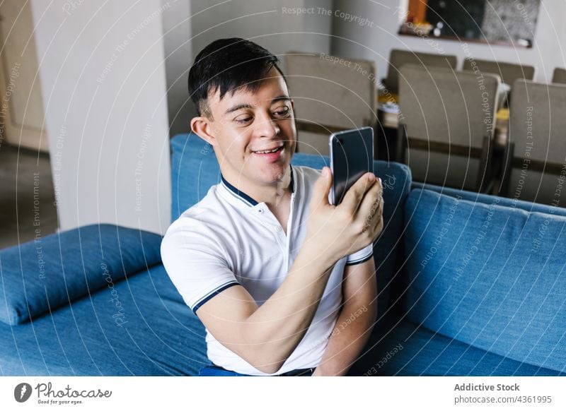 Teen ethnic boy with Down syndrome taking selfie at home down syndrome smile smartphone self portrait disorder memory moment teenage happy latin device sofa