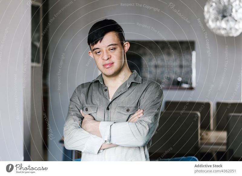 Content ethnic boy with Down syndrome standing in room at home down syndrome smile teenage arms crossed disorder happy cheerful latin casual joy positive calm