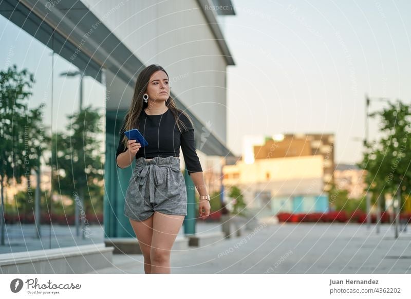 young woman walks with mobile phone in hand next to an office telephone smart phone smartphone cellular cellphone cell phone walking go lady women clock