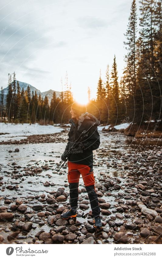 Traveler with tripod standing on river shore at sunset hiker coast forest snow explore nature season winter castle mountain banff national park alberta canada