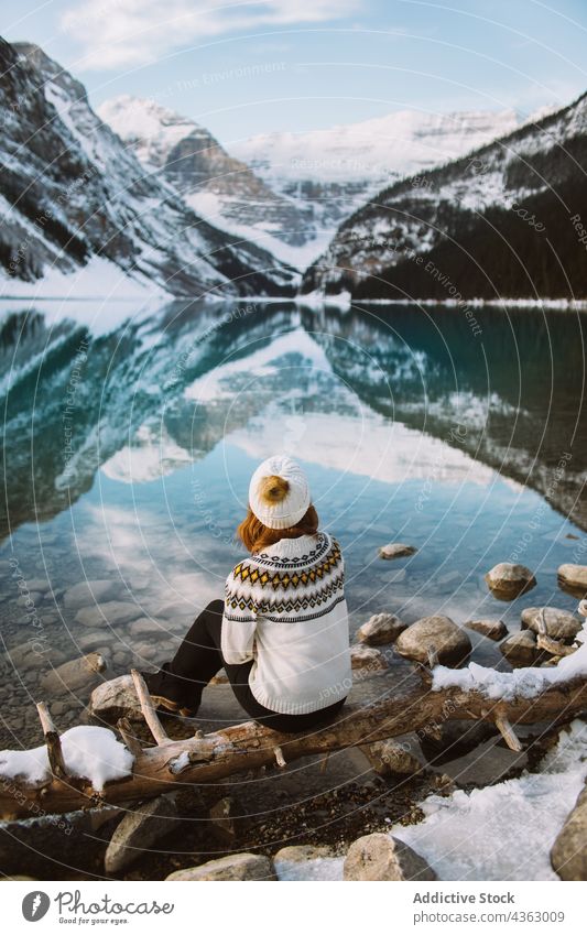 Unrecognizable woman traveler sitting near calm lake shore rest mountain nature water winter lake louise banff national park alberta pensive thoughtful female