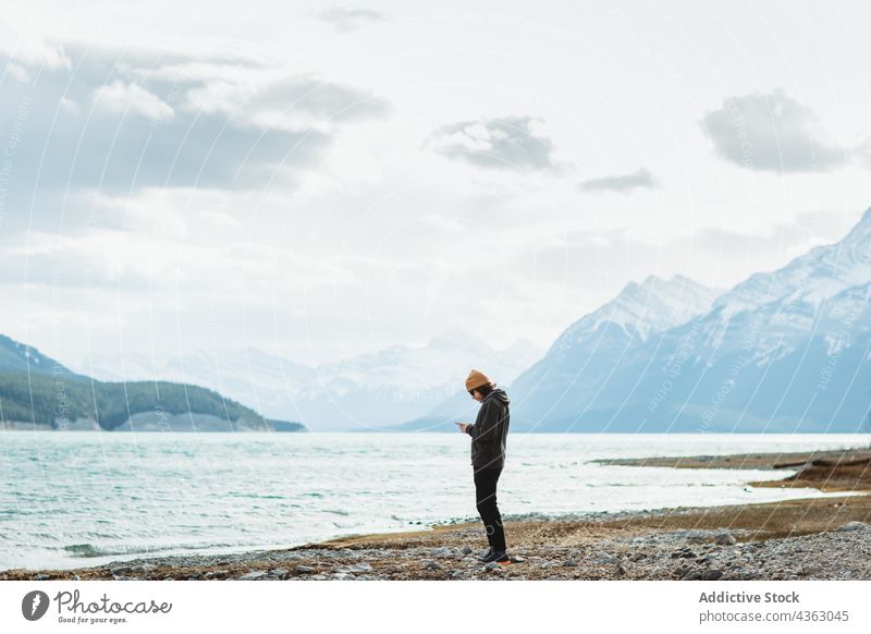 Woman using smartphone near lake woman traveler shore cloudy daytime nature water abraham lake banff national park alberta canada mountain trip tourist