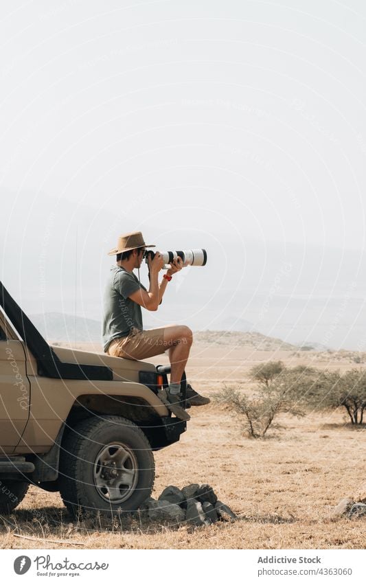 Traveling photographer taking photos during safari travel man take photo photo camera photography telephoto lens traveler male offroad off road car adventure