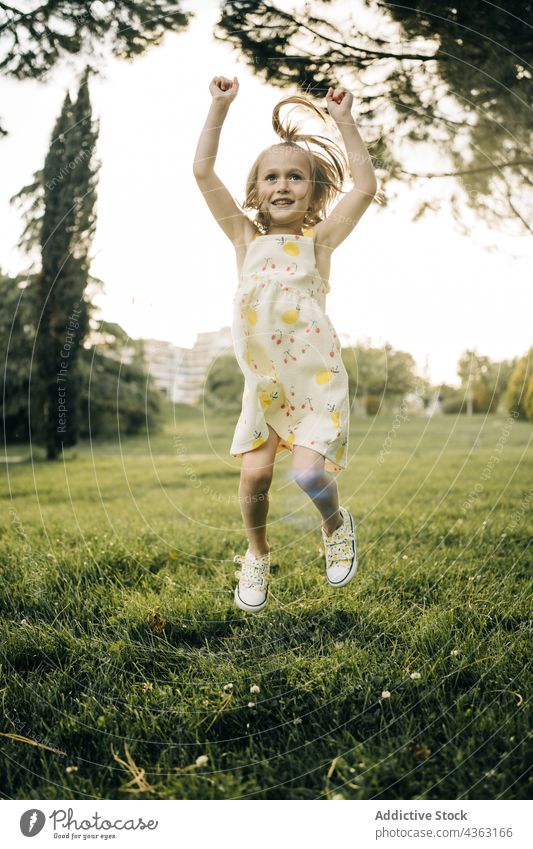 Joyful kid jumping on green meadow girl summer happy park having fun joy energy carefree cheerful child female little preschool active excited childhood playful