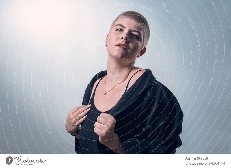 studio shot of a young, strong woman with very short blond hair in black clothes serious confident power powerful business piercing jewelry blonde portrait