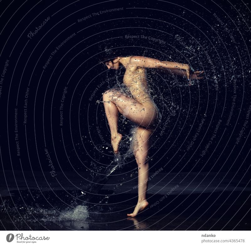 young beautiful woman of Caucasian appearance with long hair dances in drops of water on a black background. Jumping and swinging arms action active adult