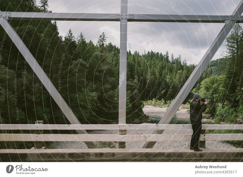 man filming video on a bridge automobiles california camera car coast forest highway mountains redwoods road steel travel