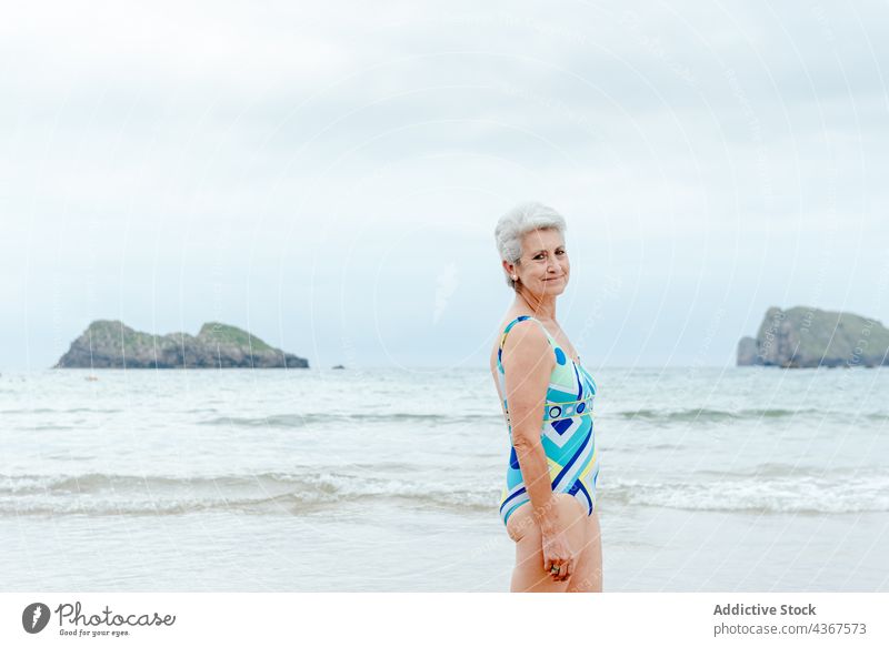 Senior woman in swimsuit resting on beach senior smile sea ocean summer happy style female aged gray hair retire wave healthy lifestyle enjoy coast swimwear