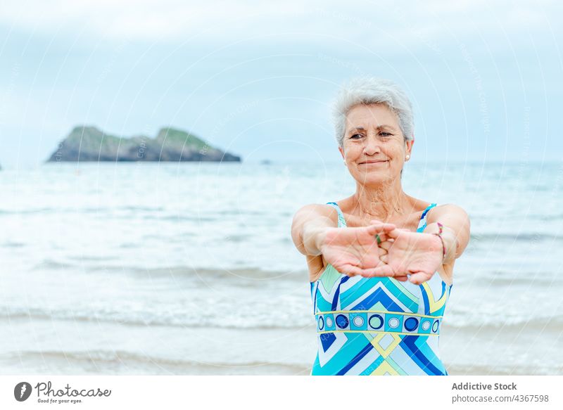 Senior woman in swimsuit stretching arms on beach senior exercise workout healthy lifestyle sea activity wellbeing female gray hair old ocean swimwear