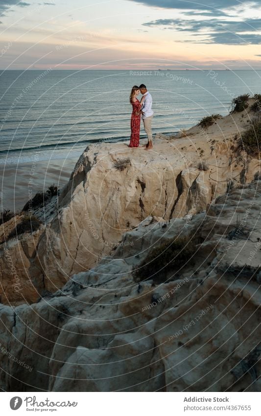 Gentle multiethnic couple standing on hill near sea at sunset embrace summer elegant romantic love together hug multiracial diverse black african american