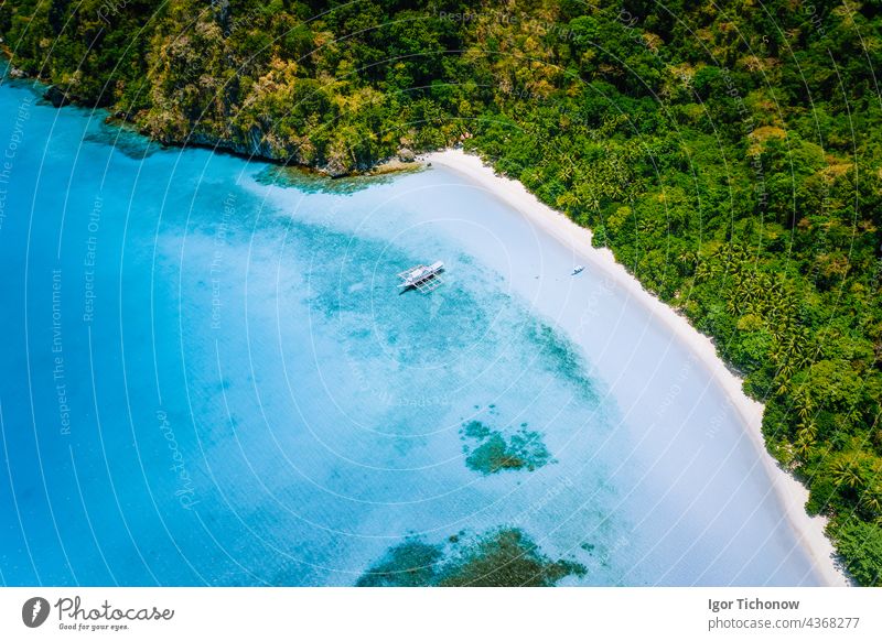 Aerial top down view of boat moored at secluded white sand beach with coconut palm trees and surreal turquoise blue shallow lagoon around. Travel exotic paradise concept