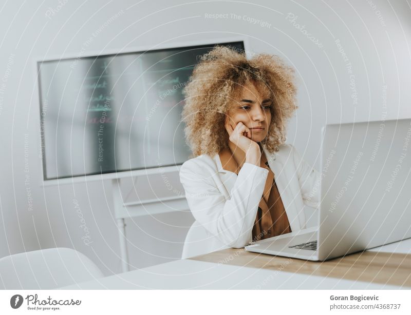 Young curly hair woman working on laptop in bright office with big screen behind her adult attractive beautiful black business caucasian communication computer