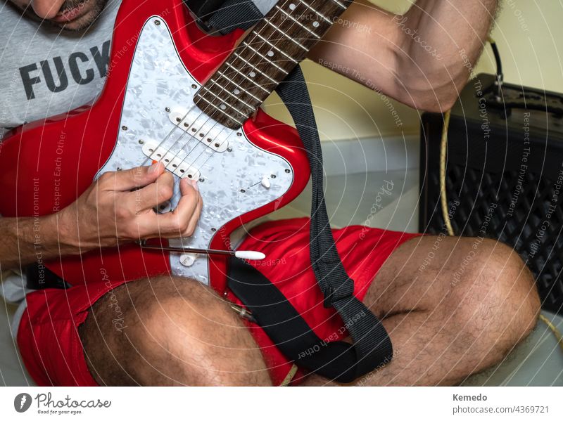 Unrecognized man sitting on the floor playing a red electric guitar. guitarist person rude male rock punk casual alternative musician player lifestyle grunge