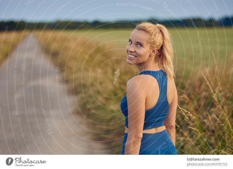 Attractive fit healthy woman turning to smile at the camera as she prepares to work out jogging along a rural footpath in a healthy active outdoor lifestyle concept