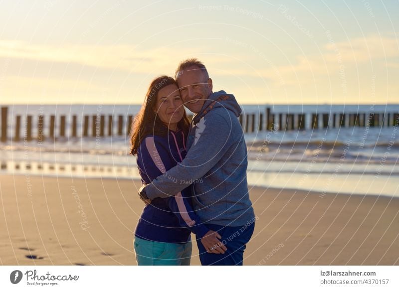 Happy romantic middle-aged couple enjoying a loving cuddle on a deserted tropical beach at sunset standing in a close embrace smiling at the camera with copy space