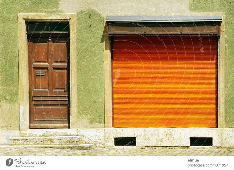 green house front with brown wooden door and large shop window with a closed orange roller shutter / company holidays / vacation house facade Facade Wooden door