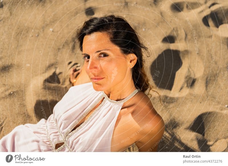 Portrait of fashion female in white dress lying on sand looking at the camera woman beach beauty portrait sunset golden leisure relax enjoy summer holidays