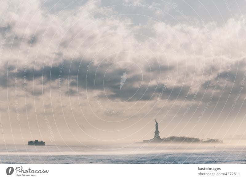 Staten Island Ferry cruises past the Statue of Liberty on a misty sunset. Manhattan, New York City, United States of America. Vertical composition. Copy space.