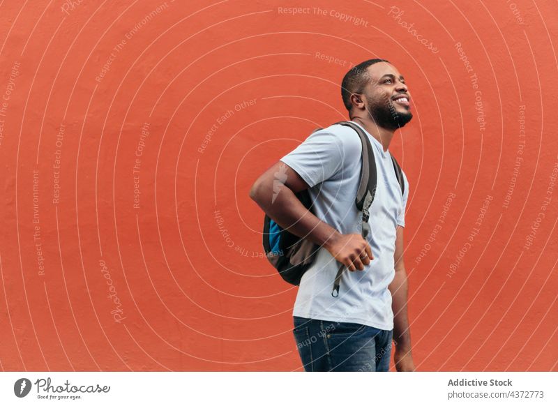 Smiling Black man with backpack looking up while standing outdoors confident male adult african american black ethnicity people walking carrying bag photography