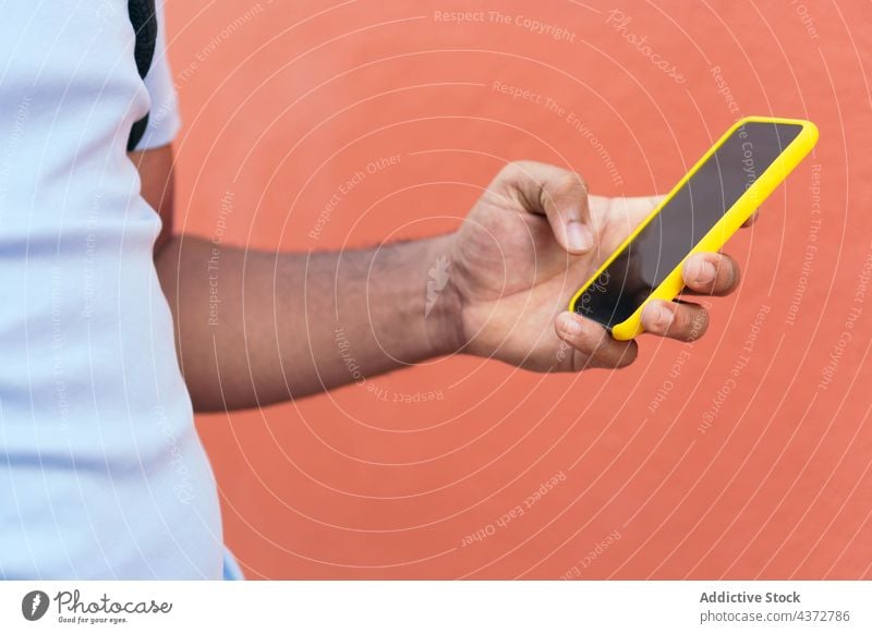 Young man with smart phone next to a red wall confident male adult african american black ethnicity technology young outdoors guy outside stylish mobile people