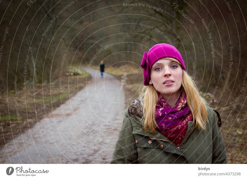 Young blonde woman with long hair and on a forest path, in the background another person in relationship. separation, feelings, partnership Young woman pretty