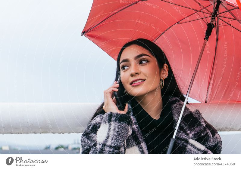 Young female using smartphone on rainy day woman street umbrella wet rest weather style ethnic young urban city browsing device gadget surfing cellphone mobile