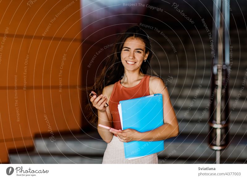 Portrait of a girl student essay in a folder, phone and glasses in her hands, hurrying to lectures stairs woman young casual smartphone university female adult