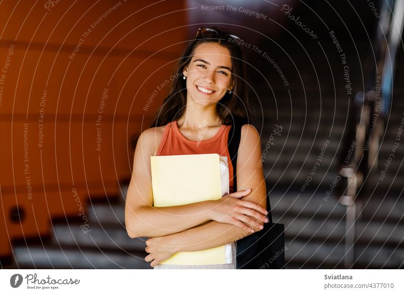 Portrait of a smiling girl with a folder in her hands student steps holding bag young university stairs glasses outdoor college woman teenager female studying